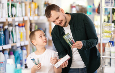 Young man with boy shoppers buying toothbrush in household chemicals store