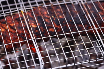 Close-up shot of a piece of meat cooking on a barbecue grill, with flames and smoke in the background.