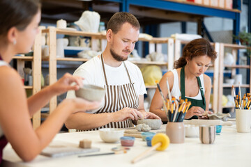 Three students in pottery workshop learn to create homemade plates and other utensils from clay