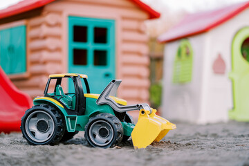 Colorful toy excavator stands with its bucket lowered on the sand at the playground