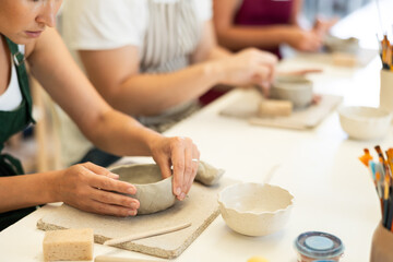 Close up girl forms bowl of clay during master class, top view. Team of creative enthusiasts is engaged in clay modeling lesson.