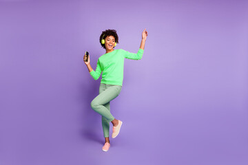 Full length body size photo of trendy stylish cute free girlfriend wearing green pants trousers yellow sweater footwear in headphones listening to music dancing isolated violet pastel color background