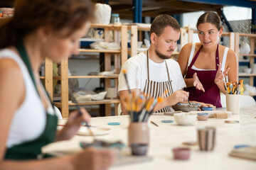 Female teacher and mentor helps students learn how to make patterns on ceramic plates using paint...