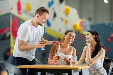 Young man approached to meet two young women sitting at table on climbing wall