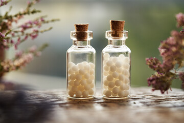 White homeopathic pills or globules in two glass bottles with pink dried flowers and herbs