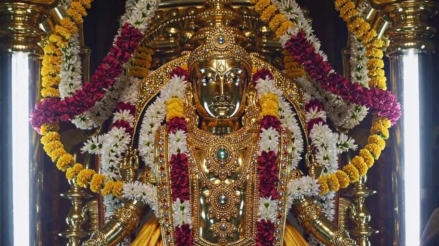 Close-up video of a richly adorned golden deity statue, draped in vibrant flower garlands, showcasing intricate craftsmanship and spiritual elegance.