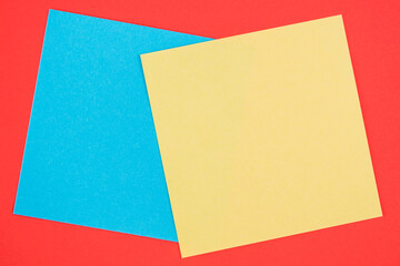 Blank memo square notes on background. Blank yellow and blue colored memo notes on red background background