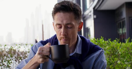 A respectable man is drinking coffee sitting on the terrace of a cafe in the city center. Sunny. day
