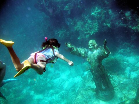 Underwater shot of a young girl snorkeling to the Christ of the Abyss Statue off Key Largo Florida Gulf of Mexico with fish swimming around and plant life growing.
