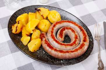 Fried potatoes and treditional spanish pork sausage butifarra on white plate