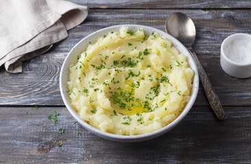 Mashed potatoes with melted butter and herbs in a gray ceramic bowl on a wooden table