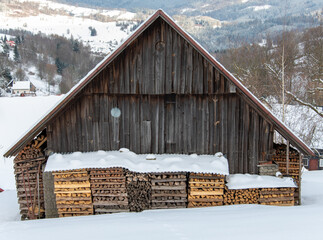 Firewood seasoning under the overhang of a snow covered barn roof in the winter, waiting to be used to heat the house when it's cold