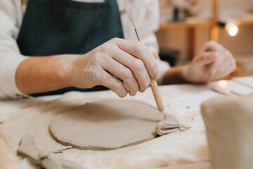 Young potter cuts a circle of clay with pottery tool in the workshop. Preparing for clay modeling, closeup.