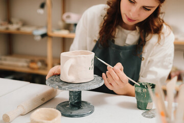 Artisan stamps decorative symbols on the dry clay of the cup. Process of designing cup with a traditional pattern.