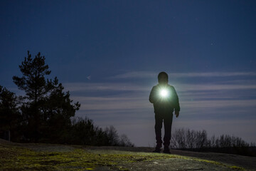 Human standing outdoor at night with flashlight and hoodie on head. Male man standing in Swedish...