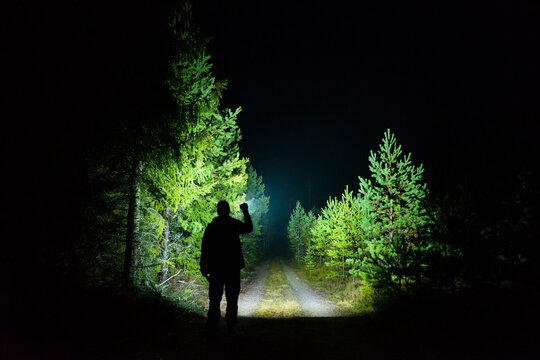 Man standing outdoor at rainy foggy night shining with flashlight. Mystical and abstract photo of Swedish nature and landscape.