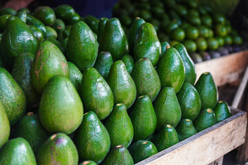 A pile of fresh avocados at a market, ready for sale. The vibrant green color and healthy look are...
