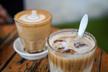 Two coffee drinks on a rustic wooden table. One is a latte with latte art, the other is an iced latte with ice cubes. Two Cups of Coffee on a Wooden Table, Latte and Iced Latte
