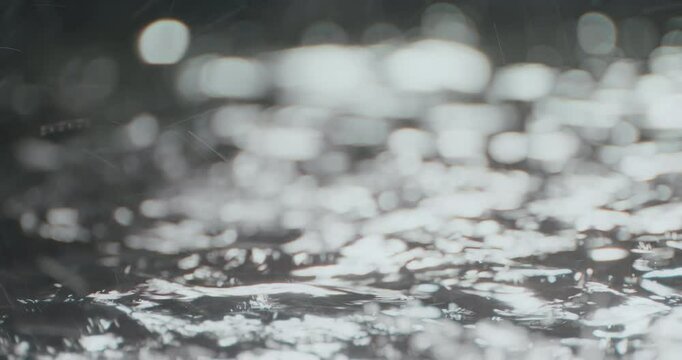 4K high-speed heavy tropical rainstorm on a black puddle floor, dynamic raindrops splashing. High-end cinematic rain closeup VFX insert, powerful weather element showcases the intense realism of rain.