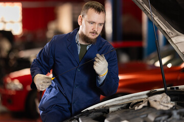 Qualified mechanic in a car service checks the amount of oil in the car with a dipstick. Car...