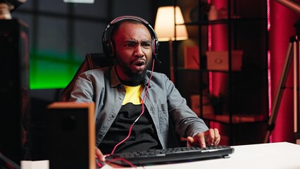Gamer wearing headphones face palming himself in frustration after getting game over message while playing videogame. Man feeling depressed while playing on gaming PC after losing, camera A © DC Studio