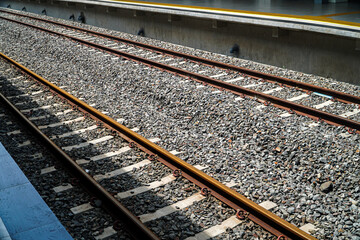 Image of train tracks at a station platform. The view is along the tracks, showing the gravel bed...
