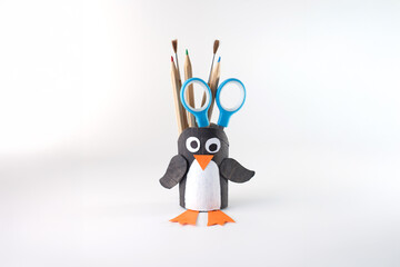 DIY penguin pencil holder made from recycled cardboard tube with scissors, pencils, and paintbrushes. with copy space. Creative desk organizer for classroom decor, kids activities, and craft tutorials © Elena
