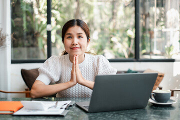 Young woman in a cozy cafe, working on a laptop, with a thoughtful expression. Natural light and greenery create a serene atmosphere.