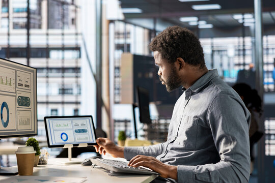 African american businessman managing administrative tasks at desk, reviewing organizational performance metrics for success. Skilled manager analyzing data focused on strategic planning.