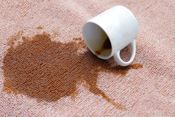 Coffee spilled from white cup on the carpet
