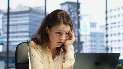 Exhausted overwhelmed businesswoman with a headache trying to meet project deadline, working hard to save the reputation of her corporation. Stressed nervous leader in crisis, overload. Camera A.