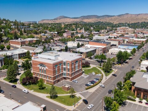 High-angle view of Klamath Falls city center, showcasing a mix of modern and historic buildings, parking lots, and greenery. Pedestrians and cars are visible.  Oregon, USA