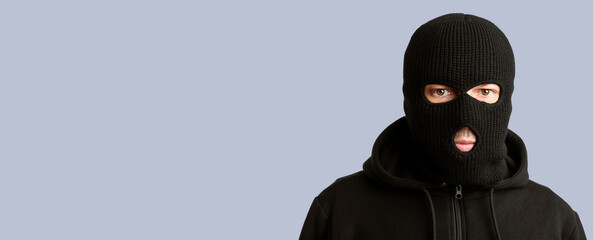 Closeup headshot of criminal wearing black balaclava and hoodie looking at camera, copy space,...