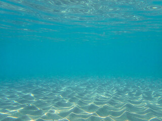 Obraz premium Dark blue ocean surface seen from underwater. Abstract waves underwater and rays of sunlight shining through, Sun light rays undersea deep, Underwater background with sea bottom, Mediterranean sea.