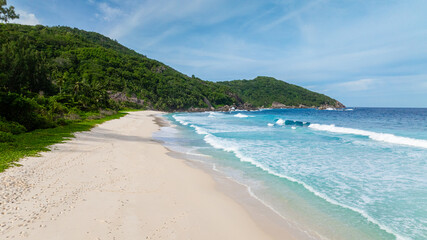 A secluded beach with white sand and footprints leading towards lush greenery and turquoise waters. Seychelles, Mahe. Police Bay.