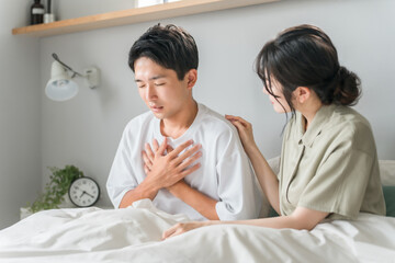朝寝室で胸痛・心臓病・肺炎に悩む男性と心配する女性・夫婦・カップル
