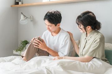Obraz premium 朝寝室で膝痛に悩む男性と心配する女性・夫婦・カップル 