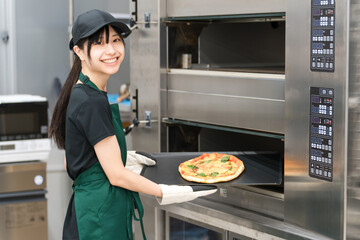 オーブンからピザを取り出す女性調理スタッフ
