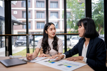 Two women are sitting at a table, talking and looking at papers
