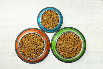 Dry pet food in feeding bowls on floor, flat lay