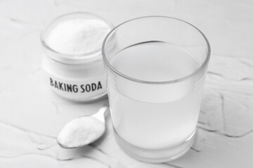 Glass with water and baking soda on white textured table, closeup