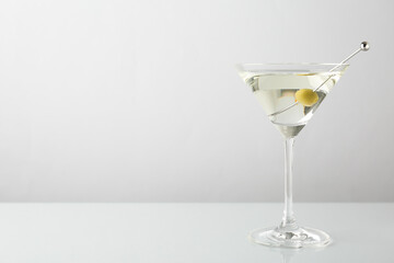 Martini cocktail with olive in glass on light table, space for text