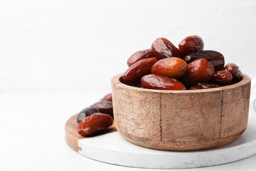 Tasty dried dates in wooden bowl on white table, closeup. Space for text