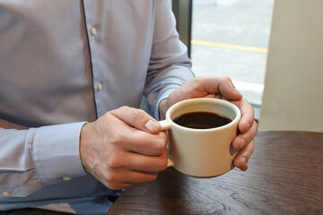 Businessman having coffee break at wooden table in cafe, closeup