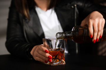 Alcohol addiction. Woman pouring whiskey into glass at table indoors, closeup