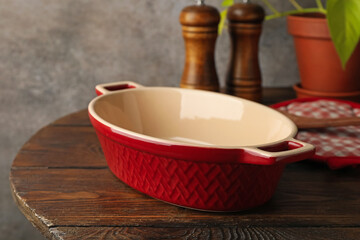 Ceramic casserole, potholder and shakers on wooden table, closeup