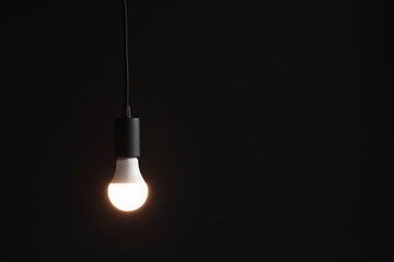 Glowing light bulb hanging on dark background. Space for text