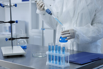 Scientist dripping blue sample into flask in laboratory, closeup