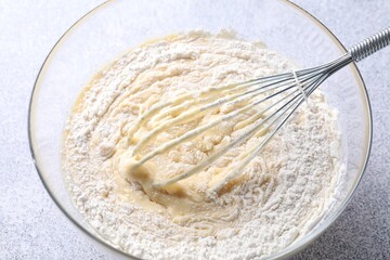 Whisk and bowl of dough on grey table, above view