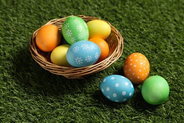 Wicker basket with decorated Easter eggs on green grass, closeup